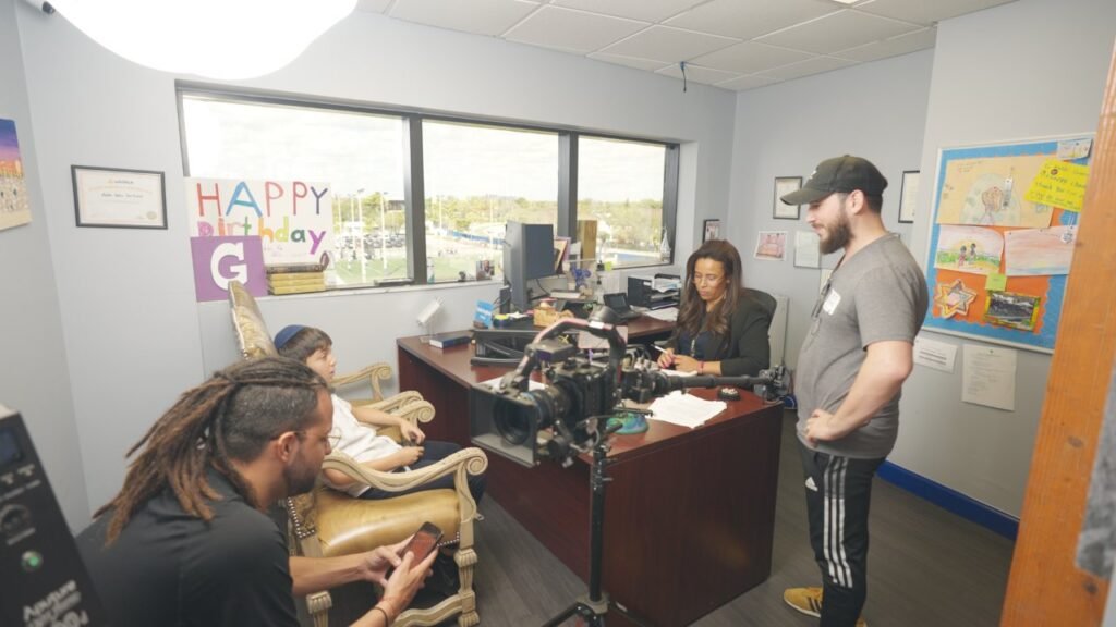 Crew filming a woman seated at a desk in a small office with paper letters on the wall