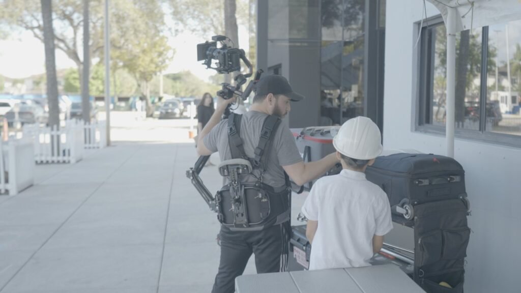 Camera operator with a gimbal rig filming a boy in a white hat on a sidewalk