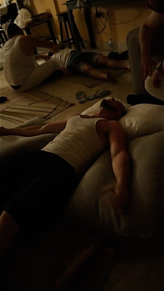 Dim room with several people lying on floor cushions and mats in low light