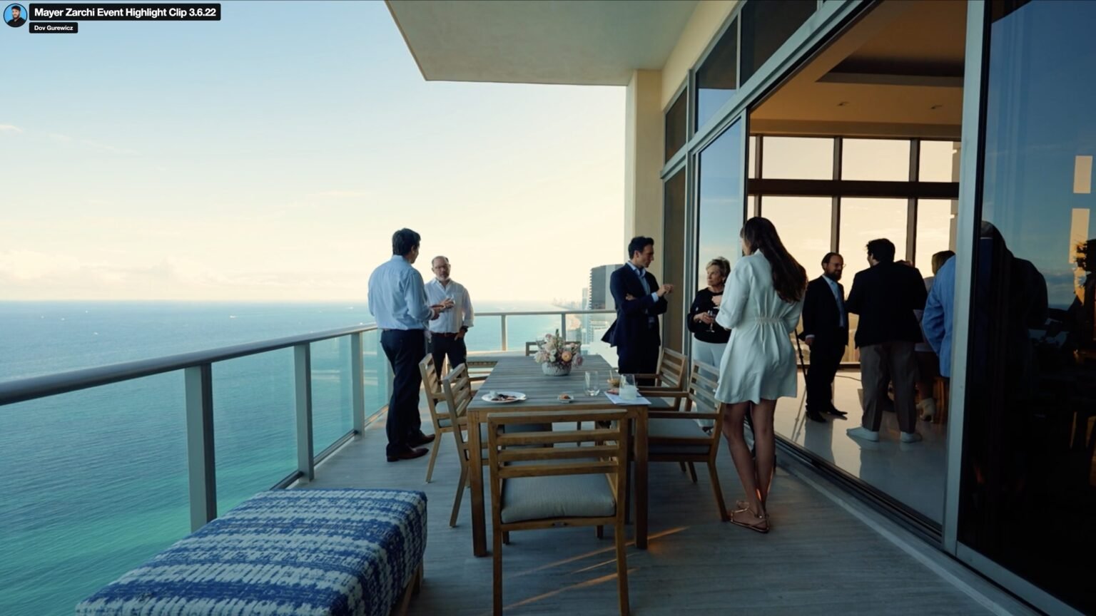 People in business attire mingling on a high balcony with dining table above the ocean