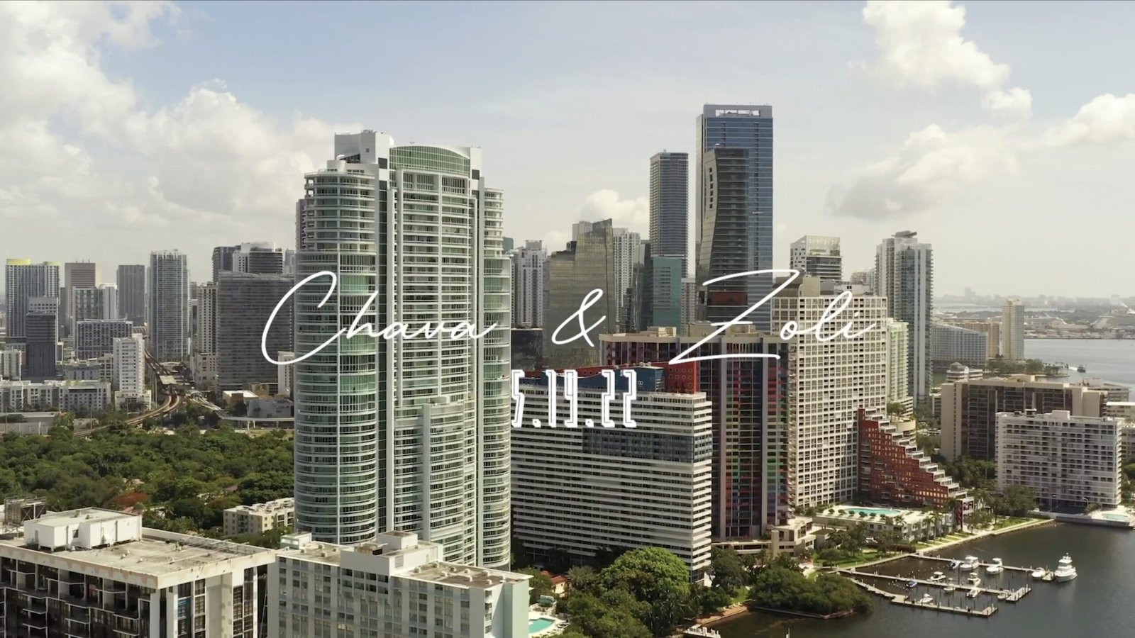 Aerial city skyline with a handwritten couple's names and date overlaid in white script