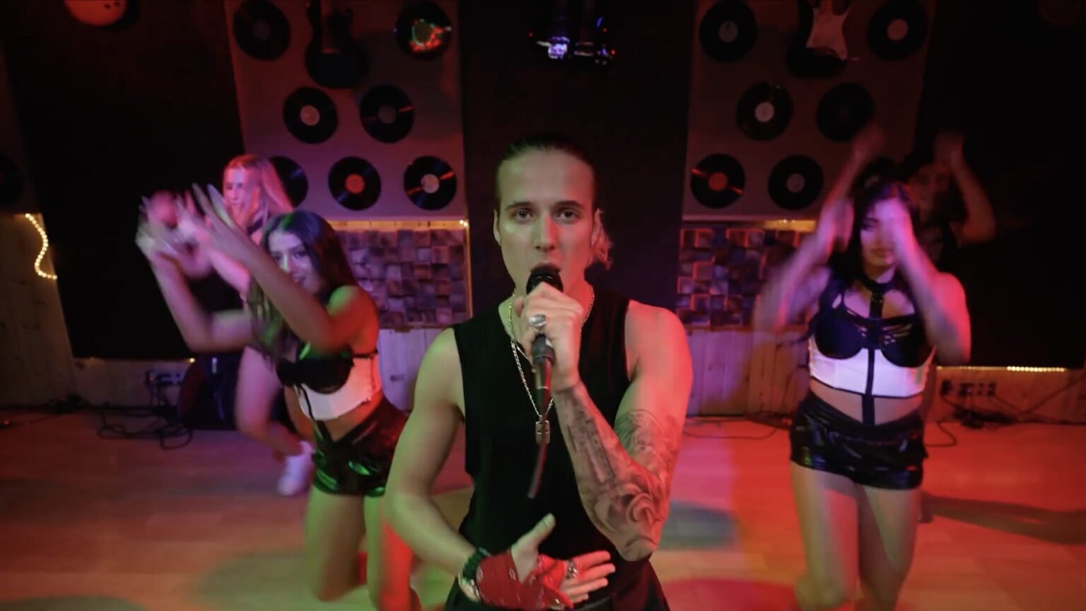 Singer holding a microphone with two backup dancers before a stage wall of vinyl records