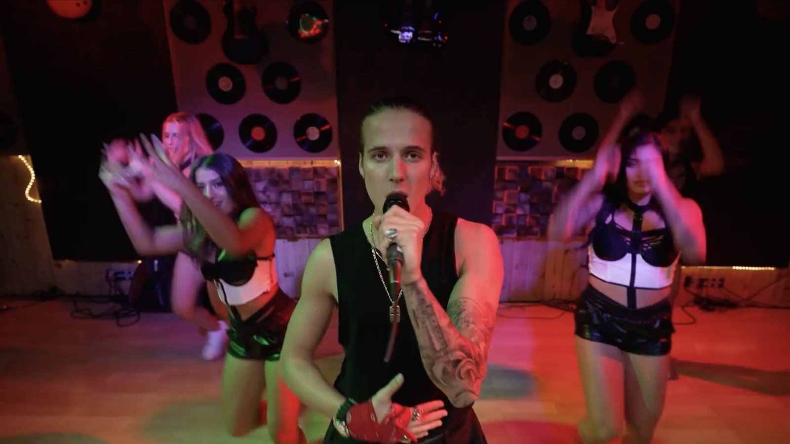 Singer holding a microphone with two backup dancers before a stage wall of vinyl records