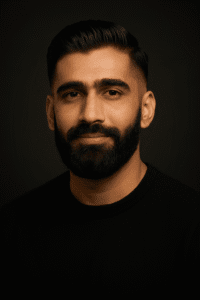 Bearded man in a black crewneck shirt facing the camera against a dark background