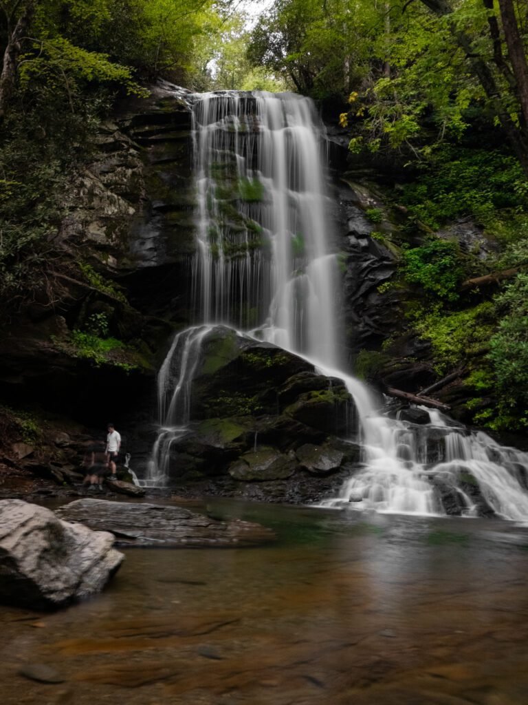 Two-tier waterfall over dark cliff rock into a clear pool ringed by boulders
