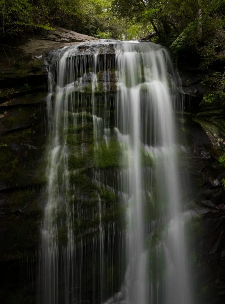 Wide waterfall fanning down a moss-covered rock face in dark forest
