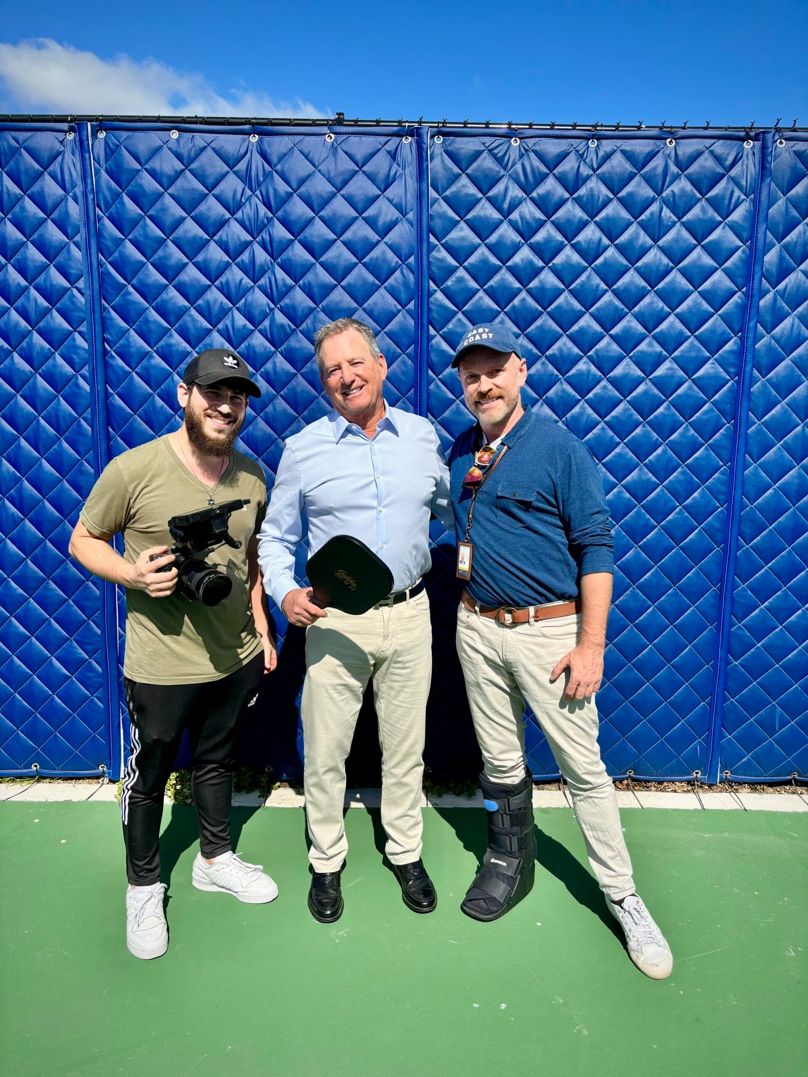 Dov Gurewicz holding a camera beside Mayor Glenn Singer and a member of the town staff on a Golden Beach court