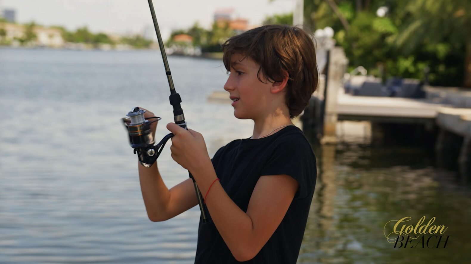 Boy in a navy t-shirt holding a fishing rod beside a waterway lined with docks