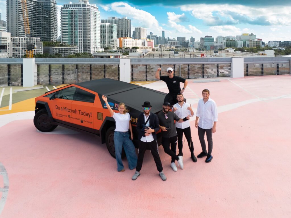 Group posing with an orange-wrapped angular pickup truck on a rooftop above a city skyline
