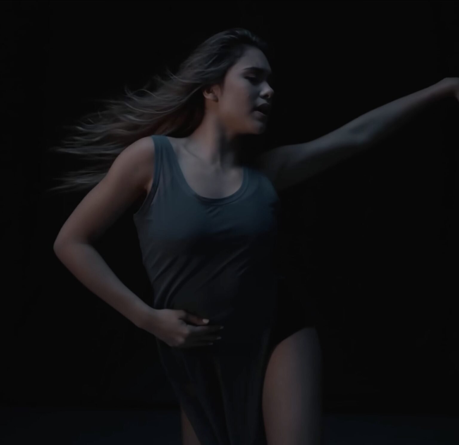 Woman in a dark leotard dancing with hair flying against a black background