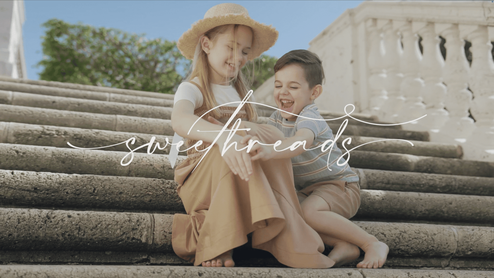 Girl in a straw hat and laughing boy sitting on stone steps under handwritten script text