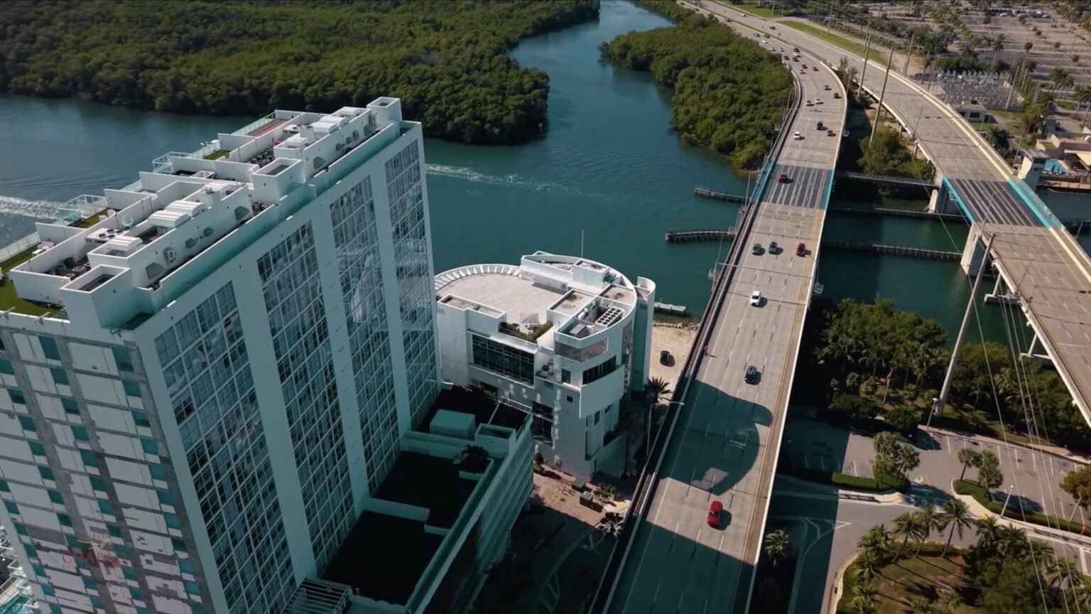Aerial view of a tall waterfront tower beside a drawbridge and highway crossing an inlet
