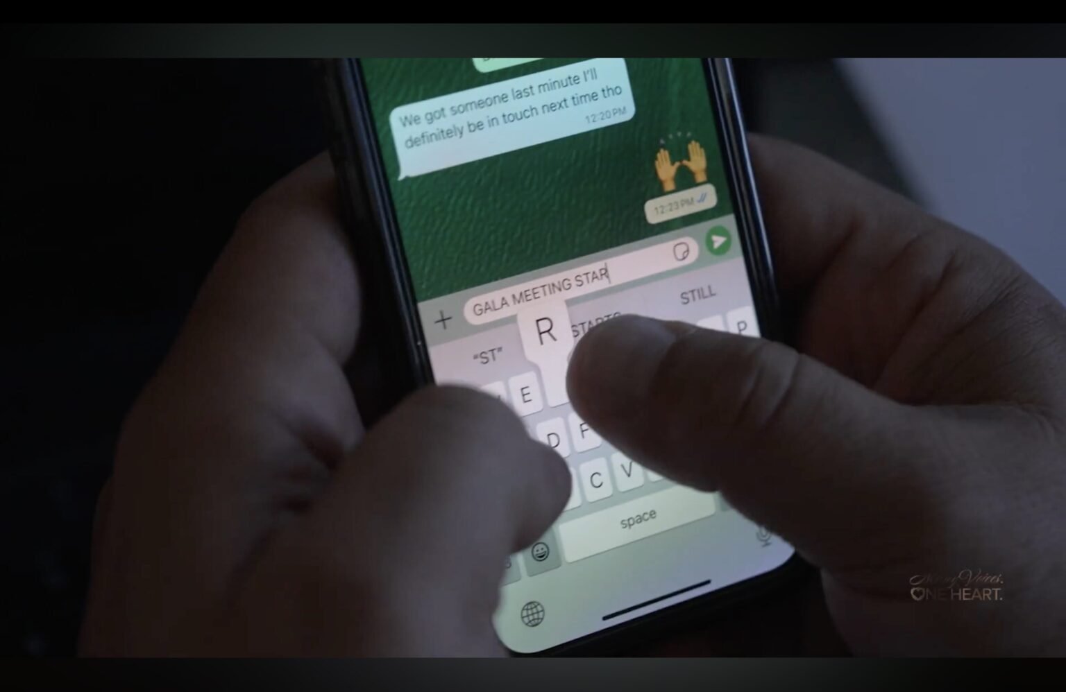 Hands typing a message on a smartphone showing a green chat thread in dim light