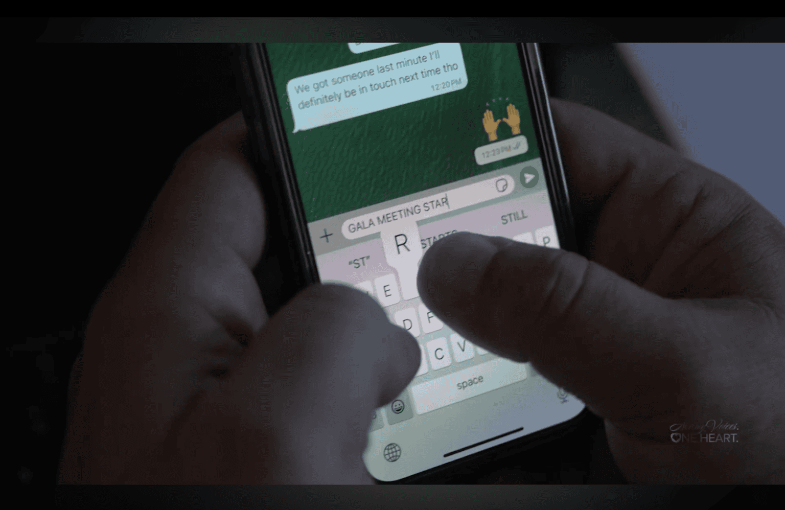 Hands typing a message on a smartphone showing a green chat thread in dim light