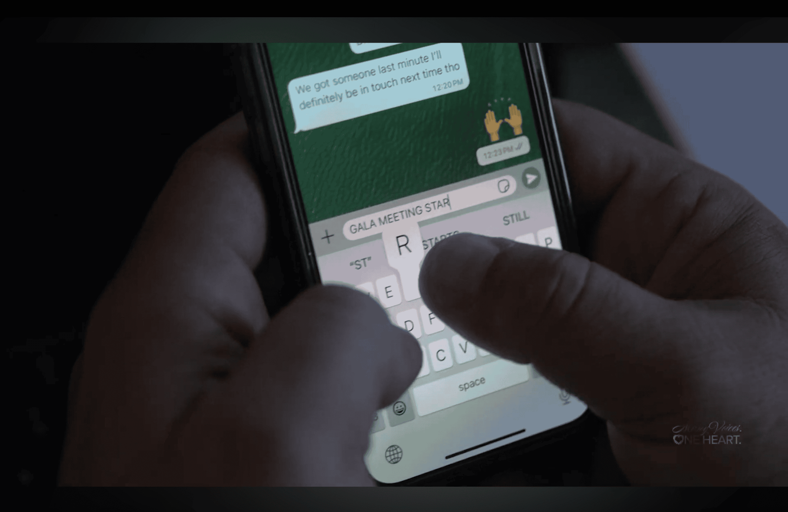 Hands typing a message on a smartphone showing a green chat thread in dim light