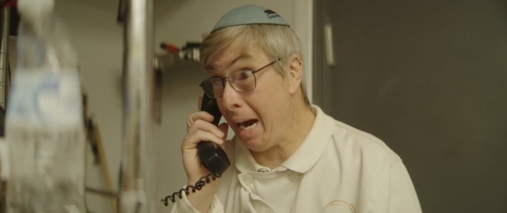 Older man in a kippah and glasses pulling a shocked face while holding a corded phone