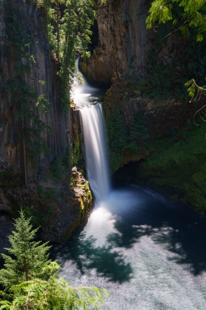 Waterfall pouring through a notch in columnar rock into a green plunge pool