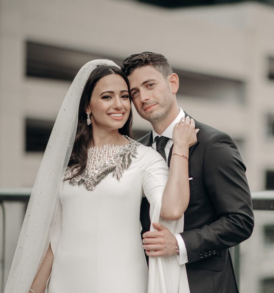 Bride with a beaded neckline and long veil leaning against a man in a dark suit