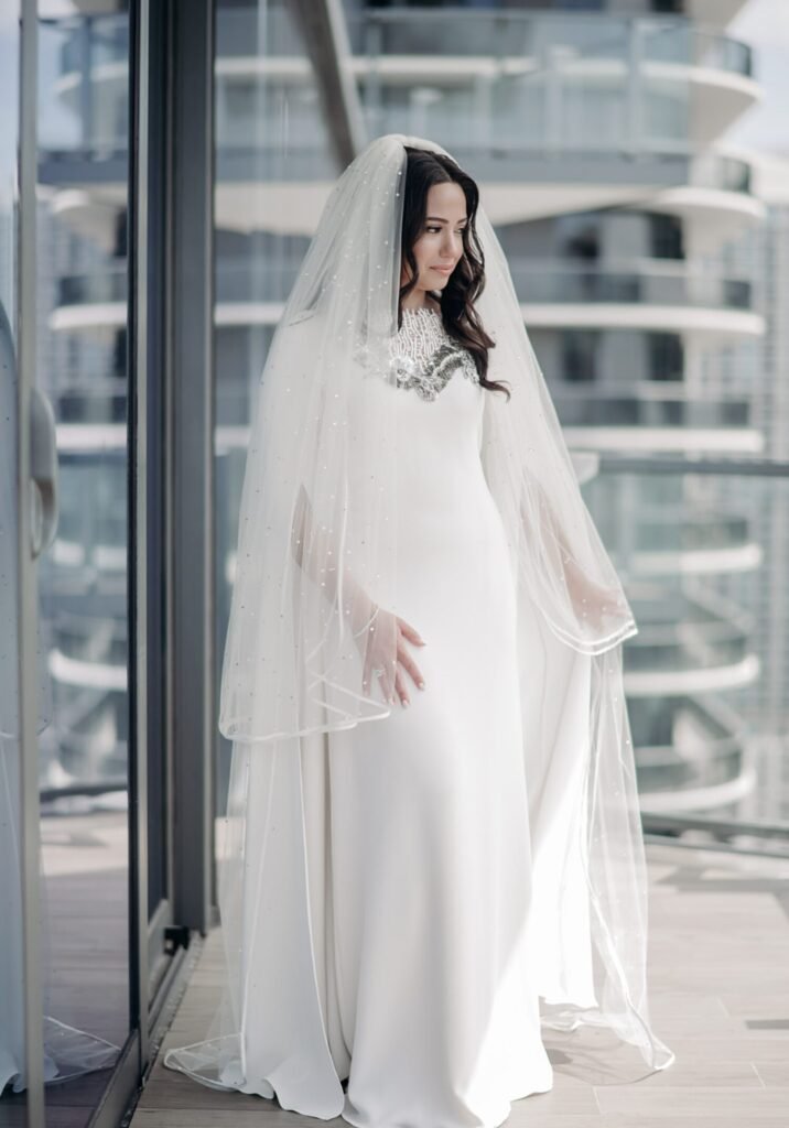 Bride in a fitted gown and floor-length veil on a balcony above curved railings