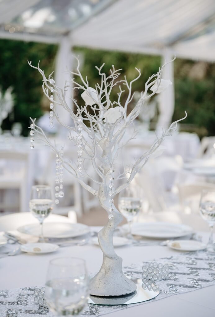 White branch centerpiece hung with crystals on a set banquet table under a tent