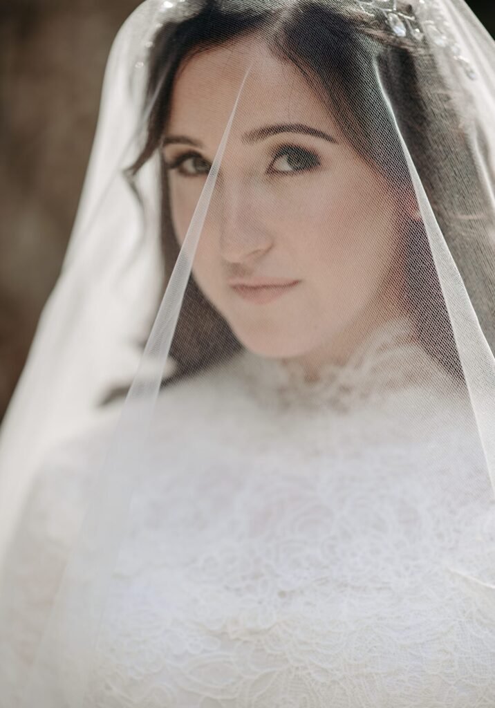 Close portrait of a bride's face seen through a sheer veil over lace