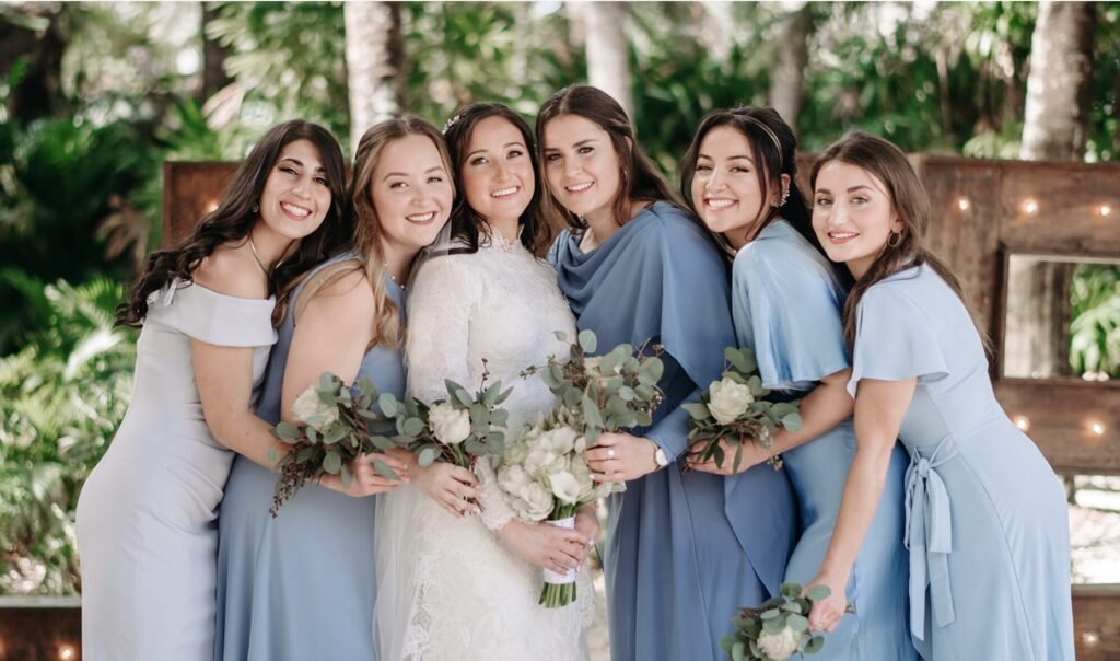 Bride flanked by five women in pale blue dresses holding white and green bouquets