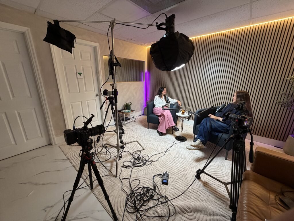 Two women seated for an interview surrounded by tripod cameras, lights and floor cables