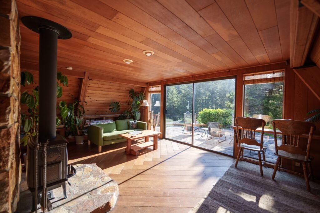 Wood-panelled living room with black wood stove, green sofa and sliding doors to patio