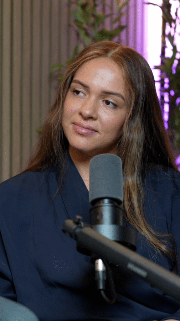 Young woman with long brown hair beside a studio microphone against a fluted wall