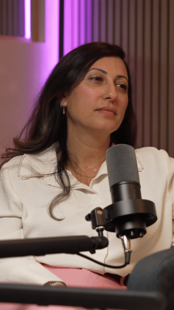 Woman in a white blouse listening beside a studio microphone under purple lighting