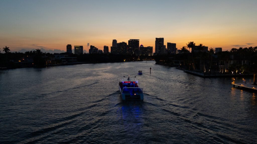 Aerial view at dusk of the Sea Rocket boat running the waterway toward the downtown Fort Lauderdale skyline against an orange sky