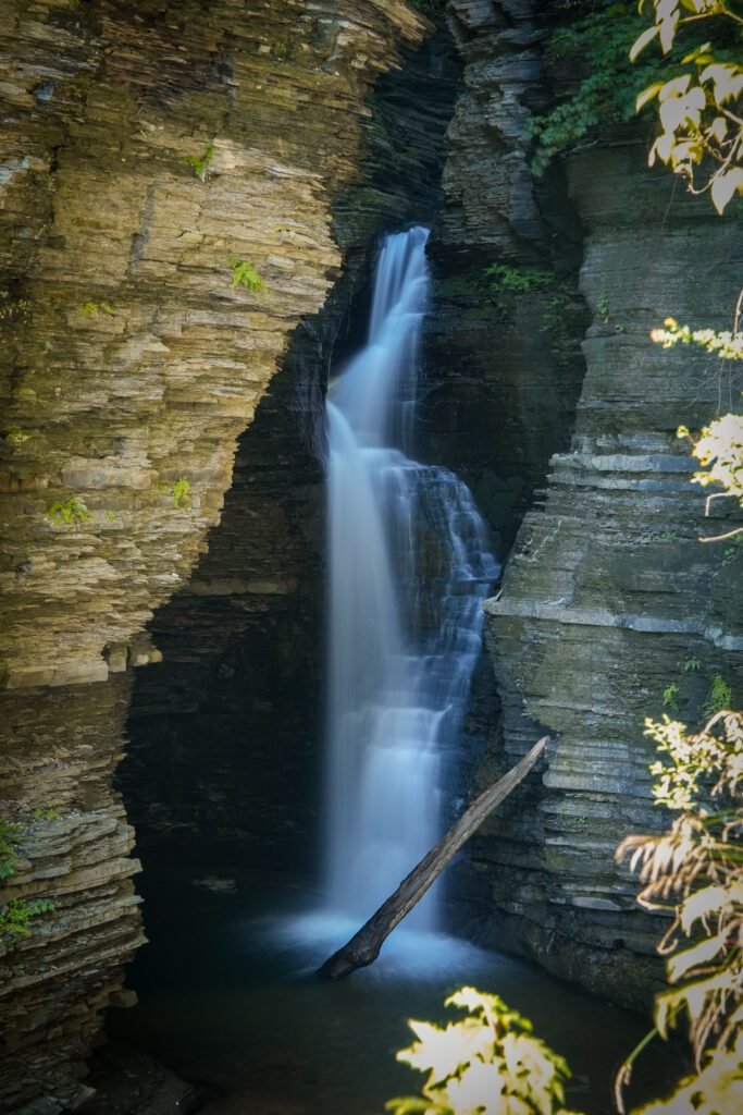 Long-exposure waterfall falling between layered shale walls into a dark pool