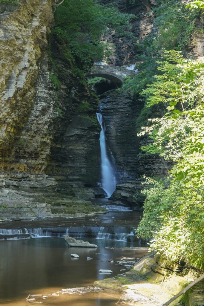 Waterfall falling beneath a curved stone arch bridge in the gorge at Watkins Glen State Park
