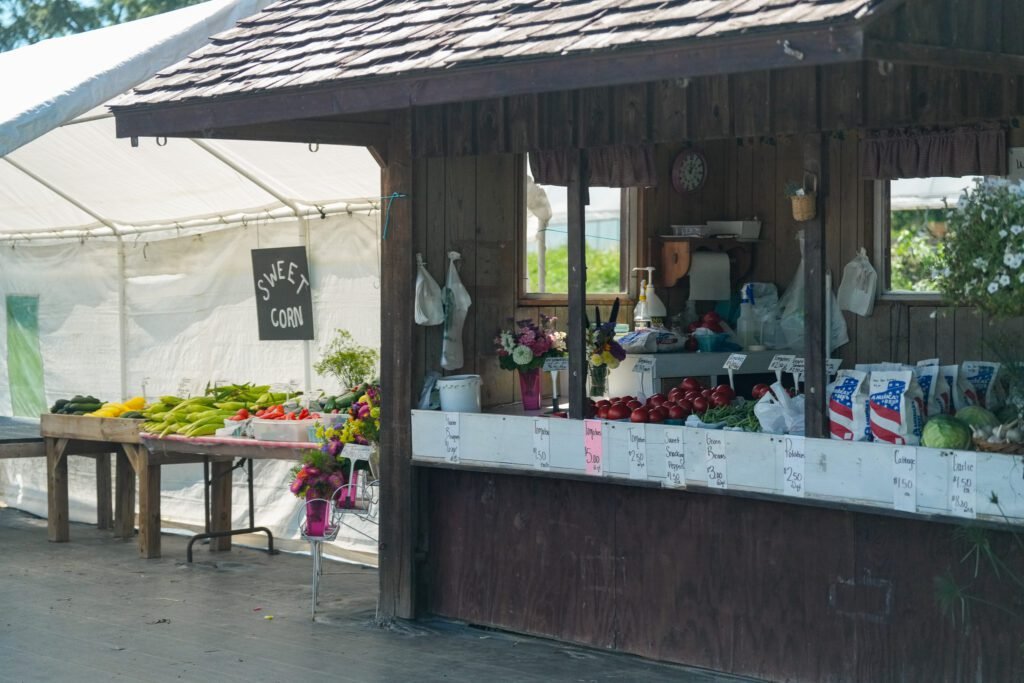 A wooden roadside farm stand with sweet corn, squash, tomatoes and cut flowers laid out for sale