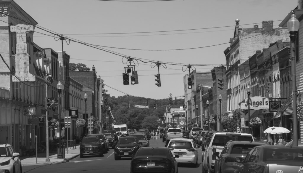 Black and white view down Penn Yan main street with traffic lights, storefronts and a sign for Lake Keuka
