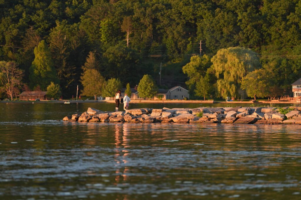Two people standing on a rock jetty on Seneca Lake in golden evening light