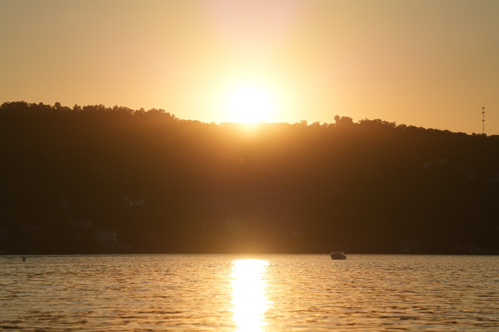 The sun setting behind a wooded ridge across Seneca Lake with a boat silhouetted on the water