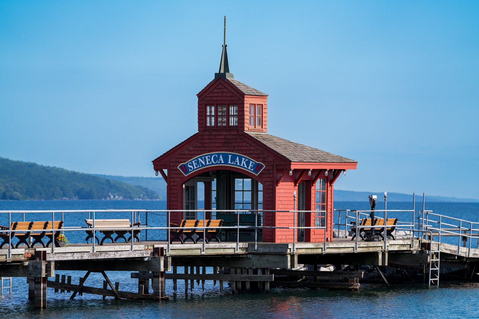 The red Seneca Lake boathouse standing on its pier with the lake and far shore behind it