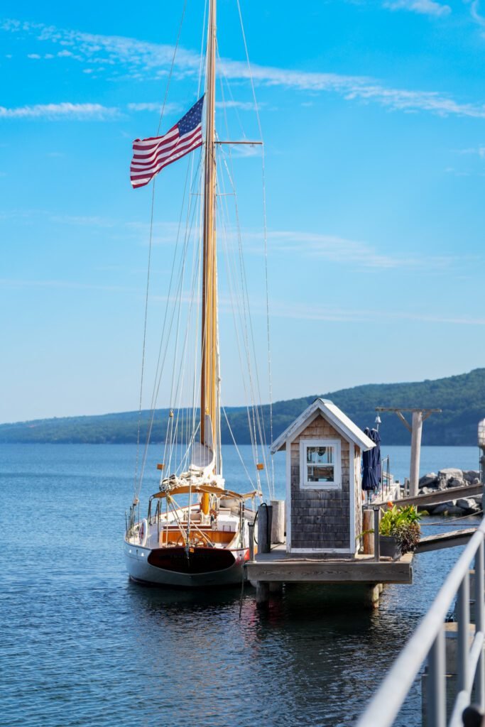 A wooden sailboat flying an American flag moored beside a shingled dock hut on Seneca Lake