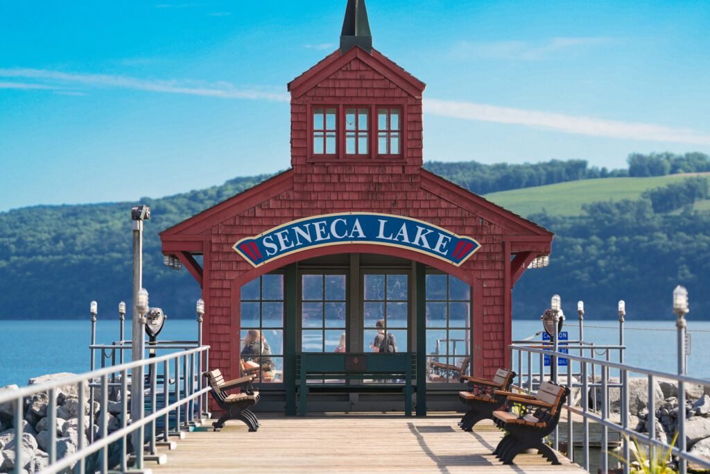 The Seneca Lake boathouse seen head on from the pier with benches either side and green hills across the water