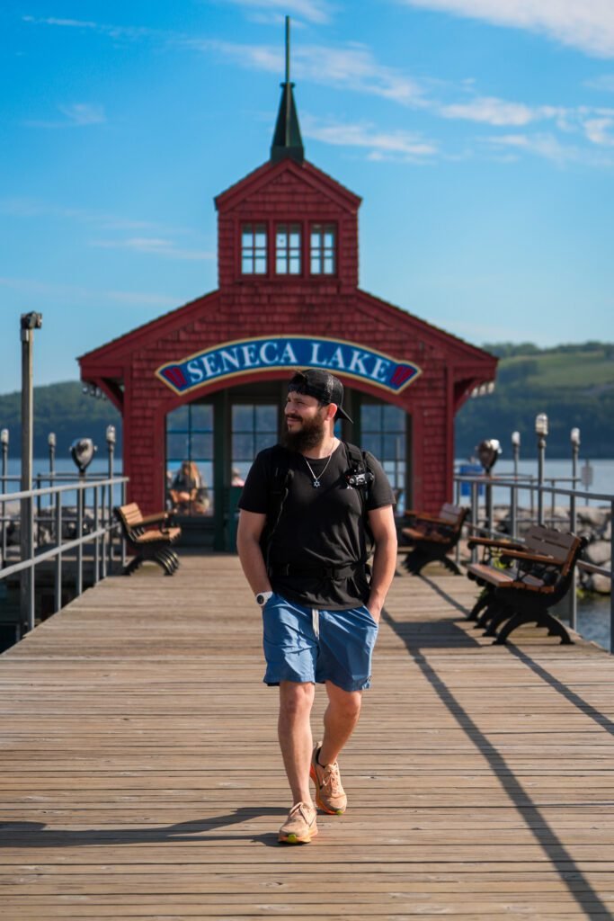 Dov Gurewicz walking down the pier at Seneca Harbor with the red Seneca Lake boathouse behind him