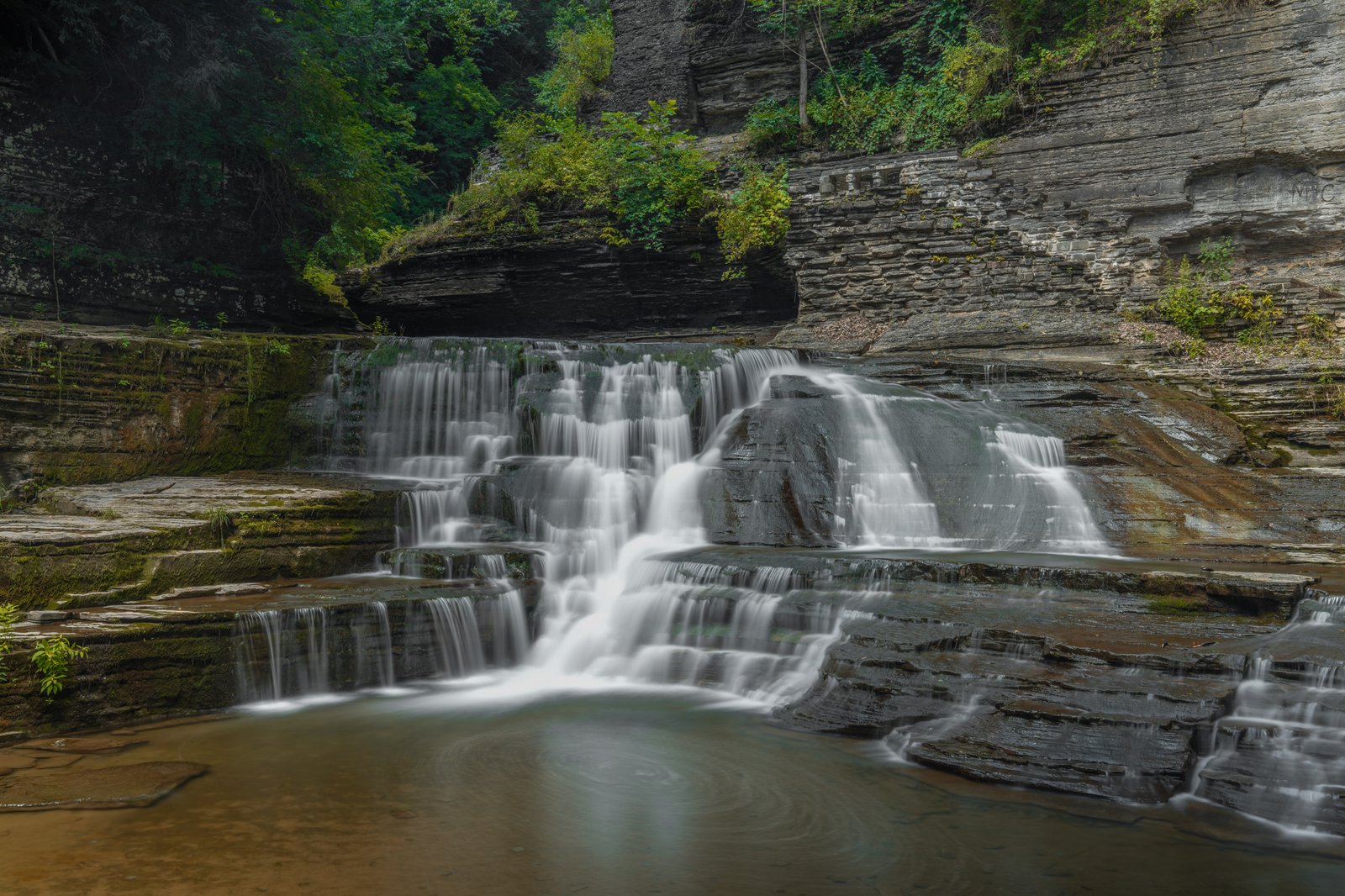 Lucifer Falls at Robert H. Treman State Park, a wide tiered cascade spreading across broad rock shelves into a shallow pool
