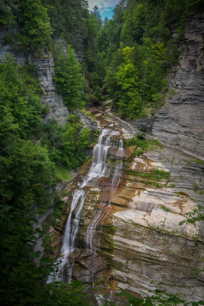 A tall waterfall falling down a pale layered cliff seen from the trail above at Robert H. Treman State Park