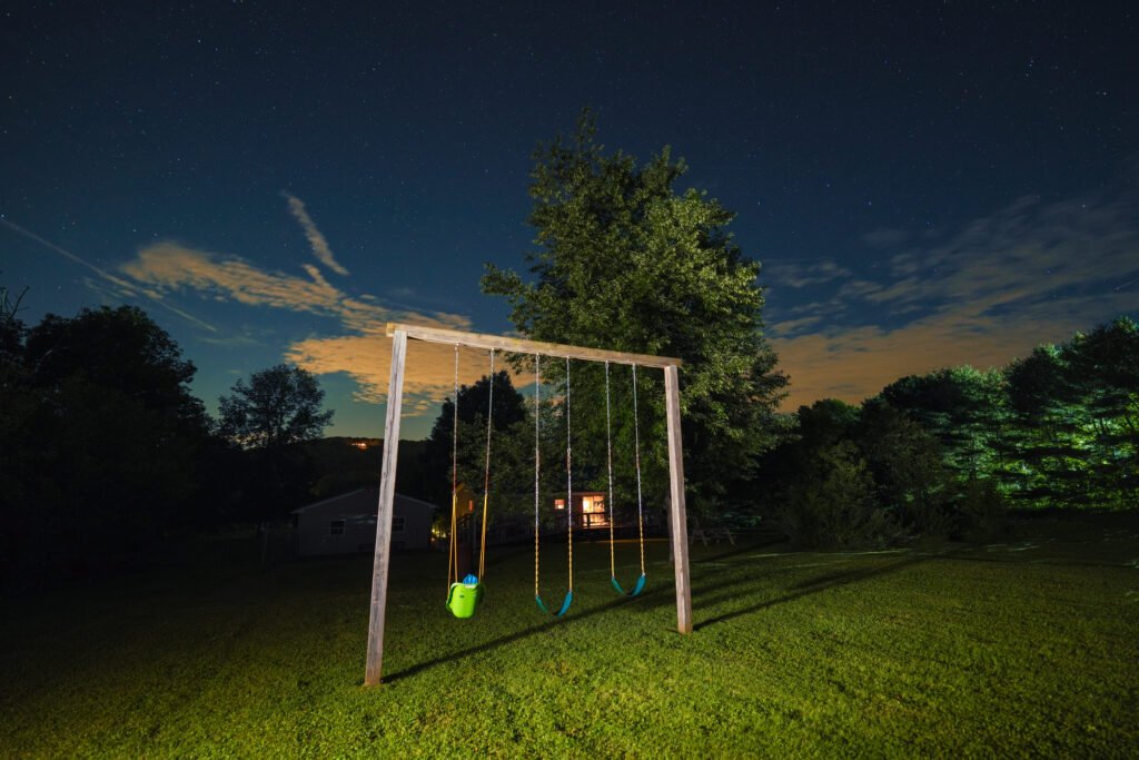 Wooden swing set on a lawn at night under a star-filled sky