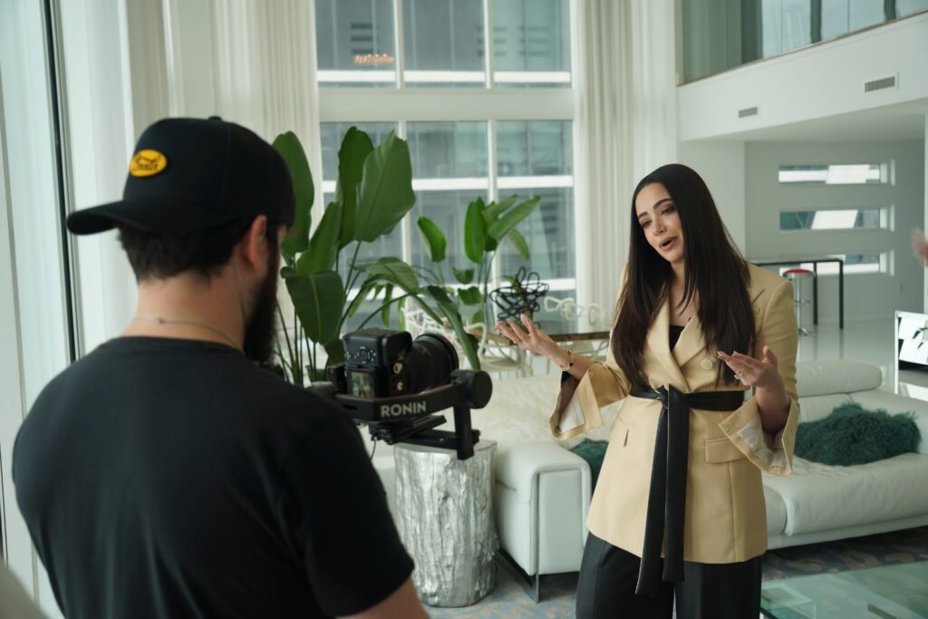 Behind the scenes filming Chava Feigen mid-sentence in a Miami condo living room, shot handheld on a Ronin gimbal