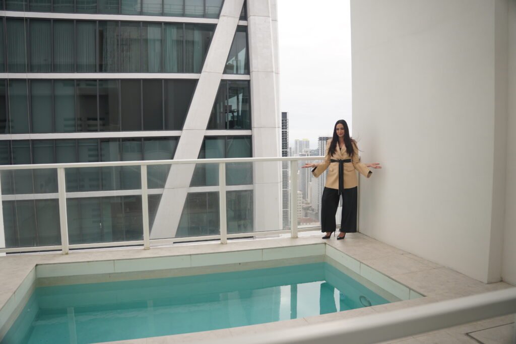 Chava Feigen presenting the private plunge pool on a high floor terrace at Ten Museum Park, the Miami skyline behind her