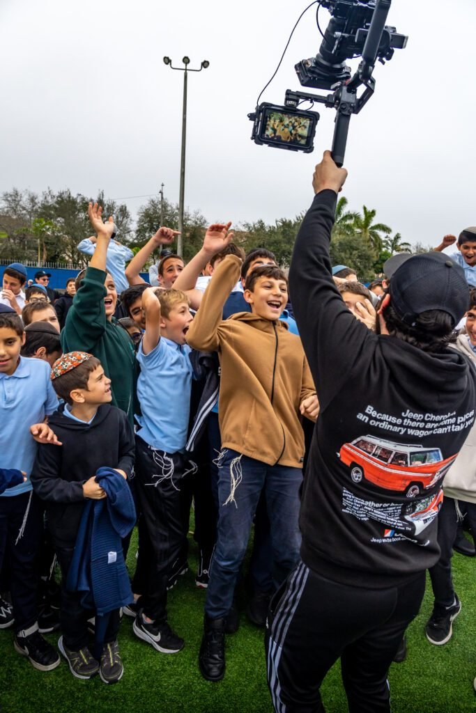 A camera operator raising a gimbal over students with their arms in the air during the Gift to the Rebbe music video shoot