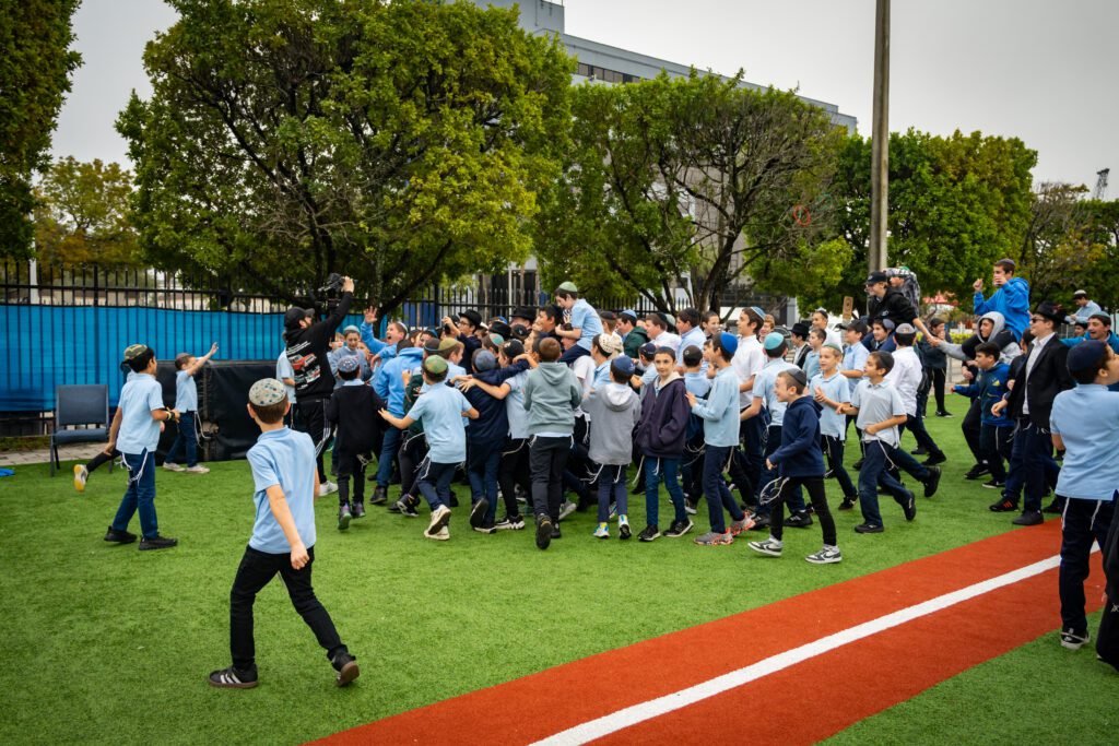 Students dancing in a wide circle on the field during filming of the Gift to the Rebbe music video at LEC