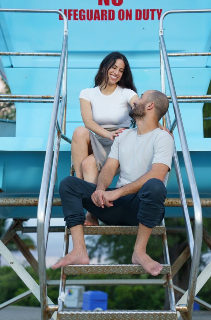 Couple on the steps of a lifeguard tower beneath a no lifeguard on duty sign