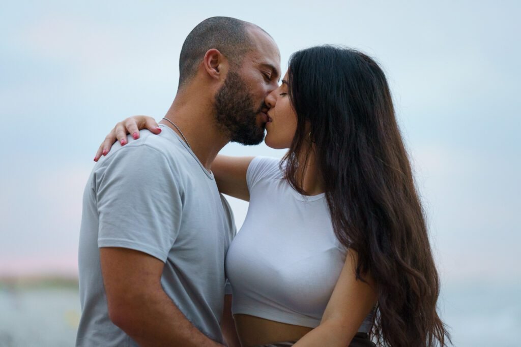 Couple kissing, her long hair loose, beach and sky blurred behind